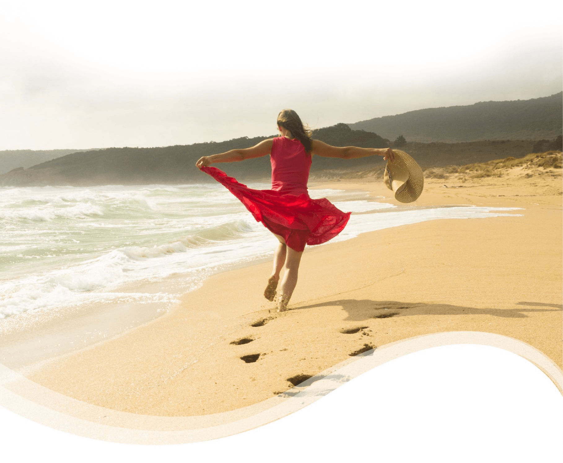 Back view of woman in red dress walking on the sea shore with arms wide open